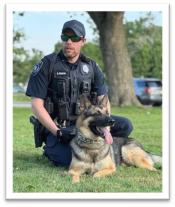 Photo of Officer Shawn Deneen in uniform and K9 Teddy sitting together in the grass.